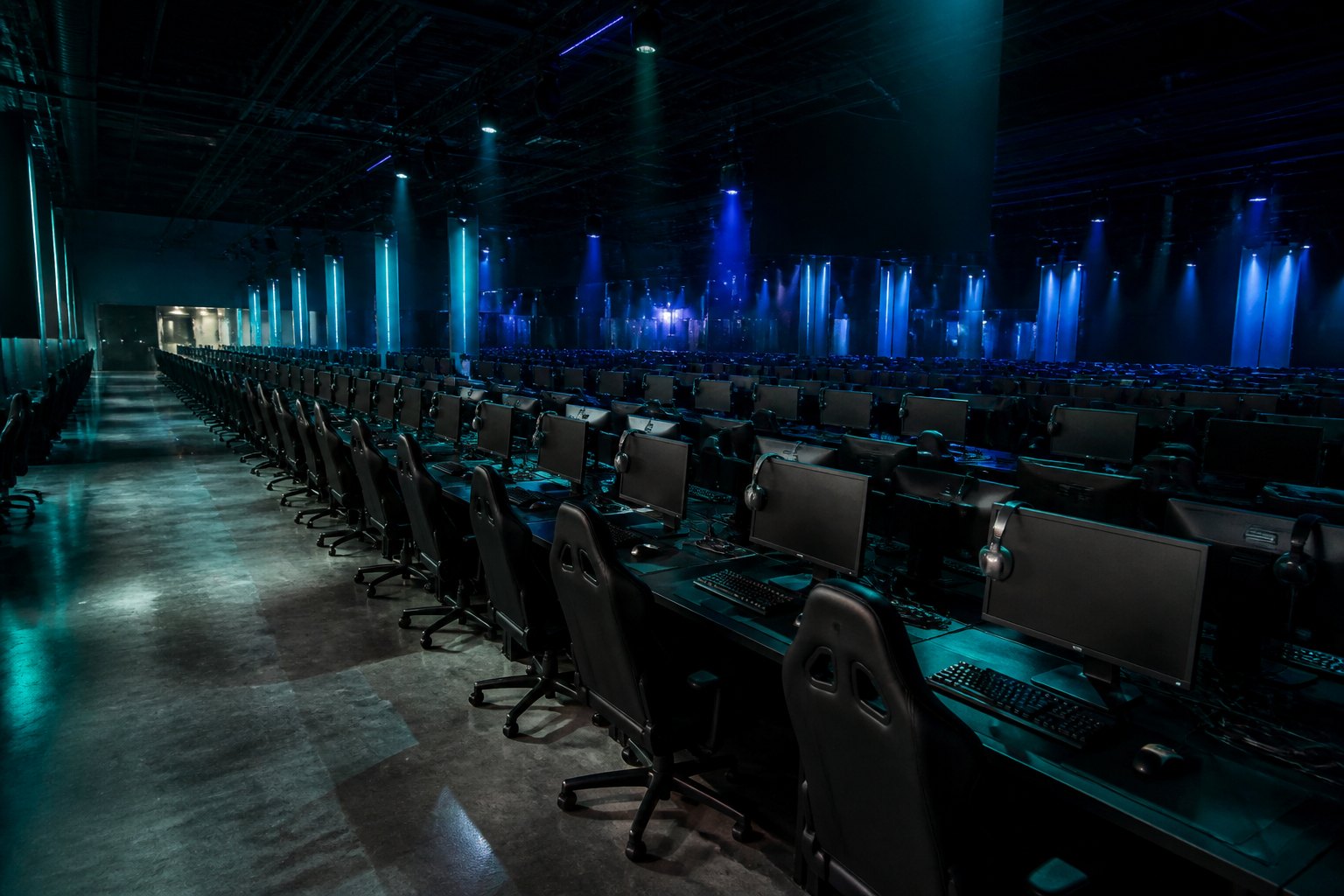 Wide view of the RESPAWN BASE hall with long rows of gaming stations under teal and indigo light